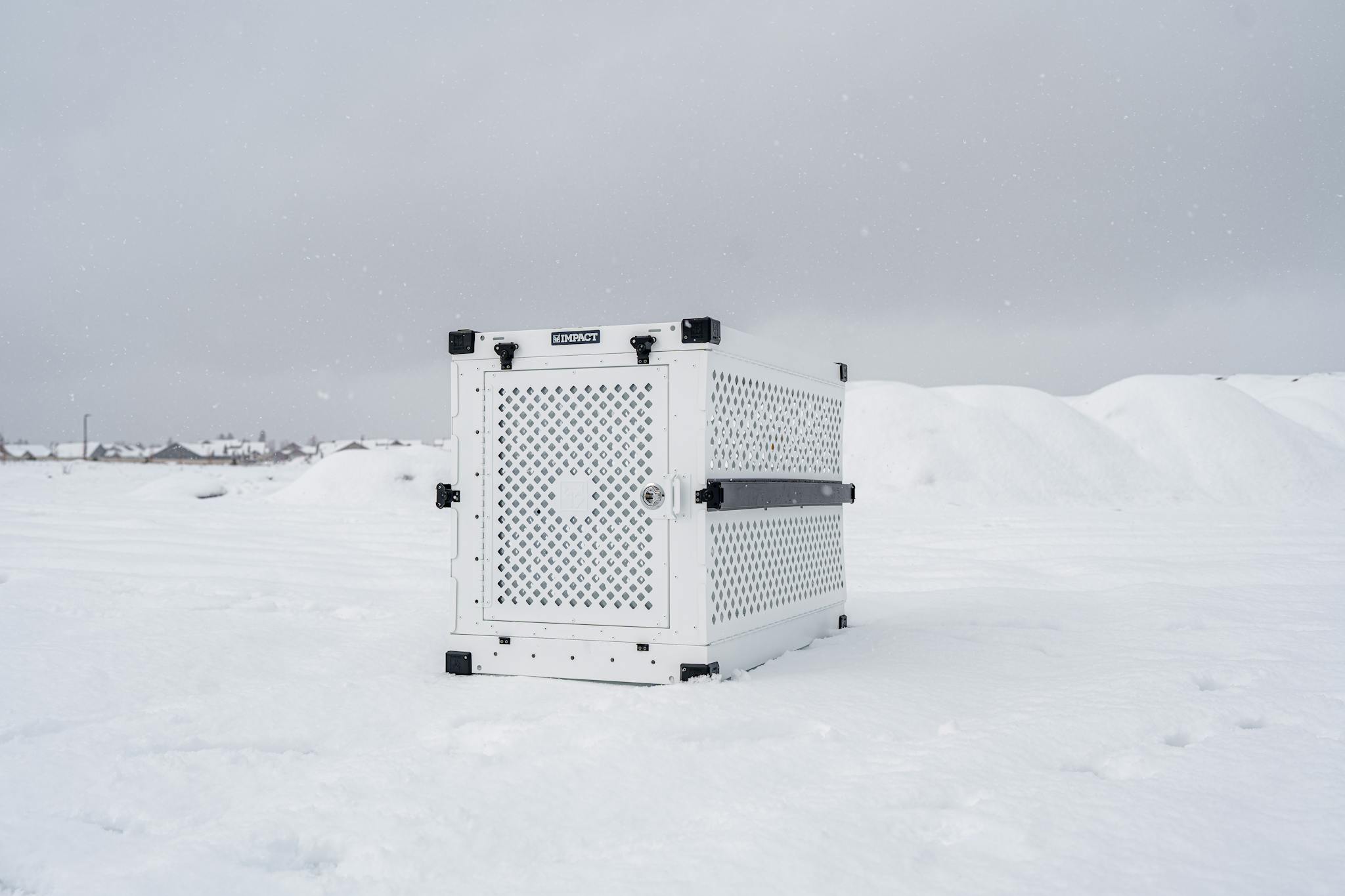 A durable Impact dog crate standing in a snowy outdoor setting, showcasing resilience.